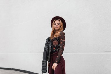 Şehirde beyaz bir binanın yanında duran siyah deri ceket zarif bir mor pelerin şapka lı vintage desenli bluz çekici genç kadın. Sevimli şık kız açık havada. Kadın giyim.