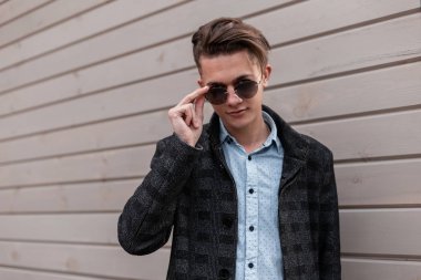 Klasik bir gömlek zarif bir gri ceket moda güneş gözlüğü şık saç modeli ile Modern genç adam hipster baharda bir vintage ahşap bina açık yakınında pozlar. Havalı erkek modeli. Erkek giyim.