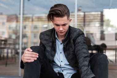 Modaya uygun bir saç modeli ile kot pantolon gri zarif damalı ceket çekici genç adam cam modern bina açık yakınında dinleniyor. Şehirde dinlenen şık adam. Moda.