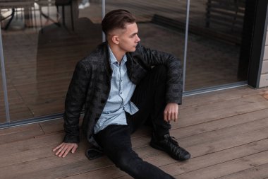 Siyah ayakkabı lı klasik bir gömlek içinde şık bir ekose ceket şık bir saç modeli ile Avrupalı genç adam modern bir binada cam kapılar yanında oturan dinleniyor. İyi adam rahatlatıcı.