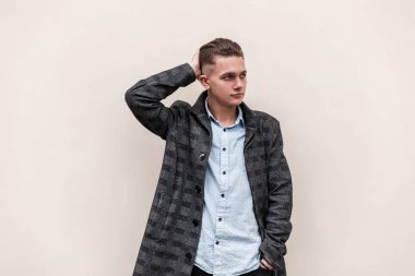 Bir kot şık gömlek gri damalı ceket bir saç modeli ile Yakışıklı modern genç adam bahar gününde şehirde beyaz bir vintage duvar yakınında duruyor. Nice Avrupalı adam açık havada.