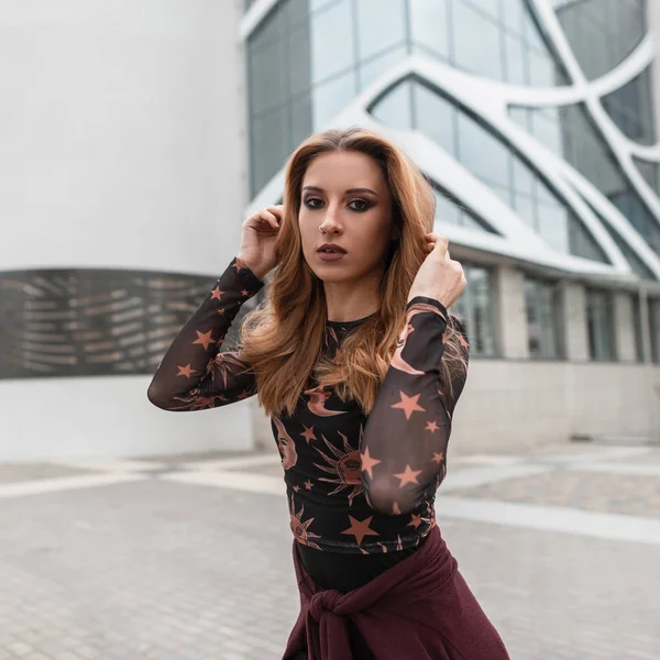 Mulher bonita ruiva com uma bela maquiagem com um brinco no nariz em uma blusa preta elegante com um padrão posando na rua perto do edifício moderno em um dia de verão. Modelo de menina sexy . — Fotografia de Stock