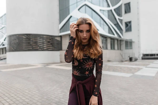 Young stylish woman with an earring in her nose with a purple cape with a trendy blouse with a pattern of the moon and stars is posing in a city near a modern building. Pretty girl model. — ストック写真