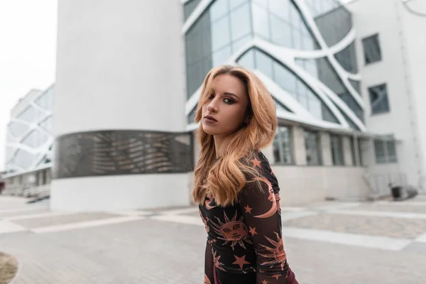 Hermosa mujer pelirroja joven en una elegante blusa con dibujos con un pendiente en la nariz con hermosos ojos está de pie en una ciudad cerca de un edificio moderno. Atractiva chica urbana modelo al aire libre . —  Fotos de Stock