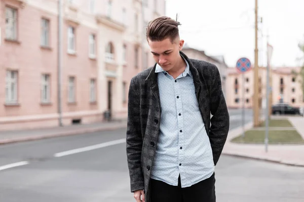 Urban stylish young guy with trendy hairstyle in fashionable elegant clothes  near vintage houses outdoors. Business guy travels through the city streets on a spring day.