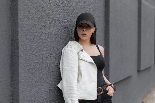 Şehirde gri bir binanın yakınında duran poz bir t-shirt vintage kot şık bir siyah beyzbol şapkası güzel güzel genç kadın. Kentsel kız açık havada. — Stok fotoğraf
