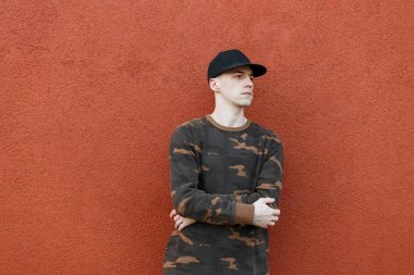 Şık bir siyah Amerikan kap şık askeri giysiler içinde Modern genç adam vintage duvarın yakınında şehirde pozlar. Bir yaz günü yürüyüşyakışıklı trendy adam. Erkek kıyafetleri. Sokak stili.