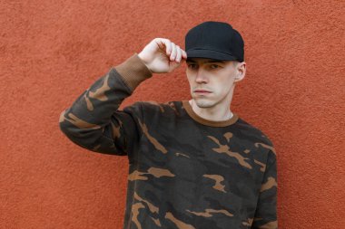 Bir vintage bina renkleri pantone yakınında şehirde poz bir trendy yeşil askeri gömlek şık bir siyah kap güzel yakışıklı genç adam. Cool çekici adam model. Sokak stili.