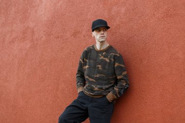 Modakot şık bir kamuflaj gömlek şık bir siyah kap modern yakışıklı adam bir vintage duvar pantone renk yakınında rahatlatır 2019 açık. Amerikan mankeni. Modaerkek giyim.