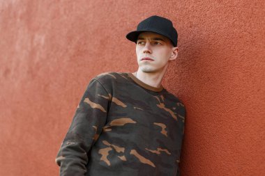 Şık bir siyah kap şık yeşil askeri gömlek Ciddi güzel genç adam bir yaz gününde şehirde bir sokakta bir pantone renkler bina yakınında dinleniyor. Yakışıklı adam modeli açık havada.