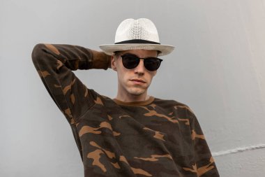 Vintage askeri gömlek şık şapka moda güneş gözlüğü Amerikan güzel genç hipster adam şehirde bir sokakta metal bir duvar yakınında pozlar. Kentsel çekici adam modeli açık havada. Yaz stili.