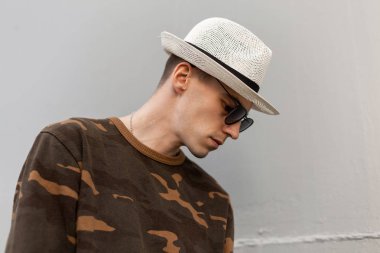 Askeri yeşil moda gömlek şık güneş gözlüğü saman vintage şapka Yakışıklı genç hipster adam metalik gri duvar açık yakınında dinleniyor. Çekici adam yaz günü sahiptir.