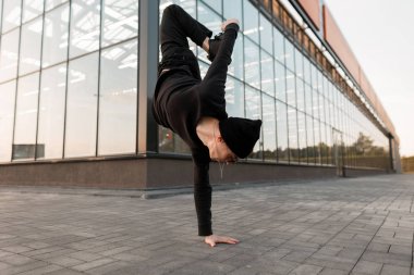 Kot pantolon şık bir gömlek spor ayakkabı siyah örme şapka lı Amerikalı genç erkek dansçı bir cam binanın yakınında açık havada dans ediyor. Yakışıklı adam şehirde bir handstand yapıyor dansçı kırmak. Sokak stili