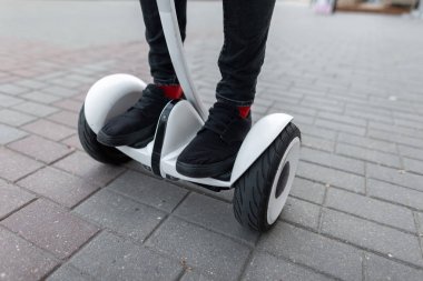 Kırmızı çoraplı spor ayakkabılı kot pantolon giymiş şık adam bir yaz gününde şehrin etrafında beyaz hoverboard üzerinde sürmek. Erkek bacaklarının ve beyaz elektrikli jiroskopun yakın çekimi. Modern teknolojiler. Aktif yaşam tarzı.