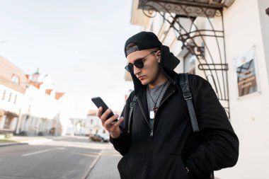 Moda şapkalı, siyah kazaklı, şık güneş gözlüklü, sırt çantalı genç, yakışıklı hippi adam binanın yanında duruyor ve telefona bakıyor. Adam şehri geziyor..