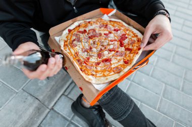 Siyah giysiler içinde Moda genç adam sıcak lezzetli pizza ve içecek cam bir şişe ile bir kutu tutuyor. Adam öğle yemeği için mola verdi. Close.