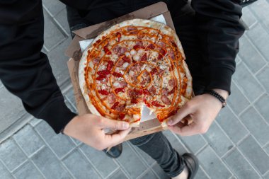 Bir adamın elinde sos lu domates ile sosis ile lezzetli sıcak pizza. Elinde pizza tutan siyah elbiseli şık adam. Yemek vakti. Yukarıdan görüntüle.