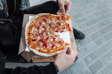 Bir adamın elinde domates ve otlar ile hardal soslu sosis ile sıcak lezzetli pizza. Elinde pizza ile şık bir adam yukarıdan görünümü. Gurme yemekler.