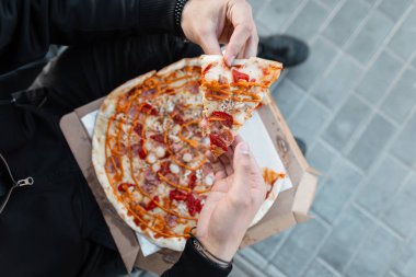 Bir adamın elinde sos lu domates ile sosis ile taze lezzetli sıcak pizza. Elinde pizza tutan siyah elbiseli şık adam. Öğle yemeği vakti. Yukarıdan görüntüle.