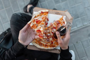 Lezzetli bir pizza ve soda cam bir şişe ile siyah giysiler içinde genç bir şık adam üst görünümü. Elinde pizza tutan serbest çalışan adam. 