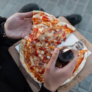 Genç adam el ele tutuşuyor sıcak lezzetli pizza ve cam şişe. Modayı takip eden adam öğle yemeği molası verdi. Yakın plan..