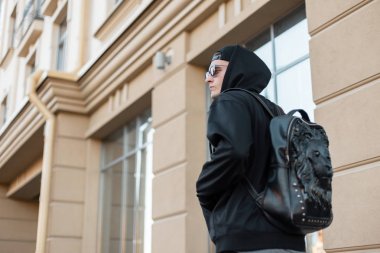 Siyah modaya uygun giyinmiş, şık deri çantalı genç hippi adam klasik bir binanın yanında sokakta yürüyor. Sıcak bir yaz gününde turist şehrin her yerine seyahat eder. Arka plan