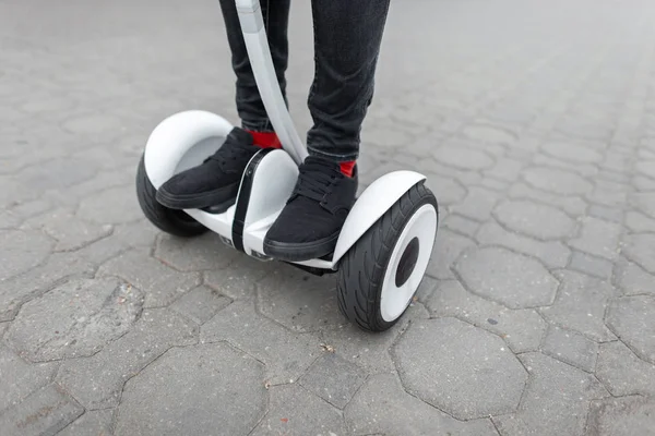 Man's legs in jeans in fashionable black sneakers riding on a gyroscope. Guy on the hoverboard outdoors in the city. Close-up. — Stock Photo, Image