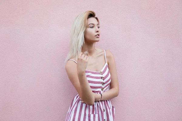 여름 세련된 줄무늬 원피스에 도시 예쁜 젊은 금발 의여자는 도시에서 분홍색 빈티지 벽 근처에 달려있다. 야외에서 귀여운 도시 소녀 모델입니다. 세련 된 여성 의류입니다. 여름 스타일. — 스톡 사진