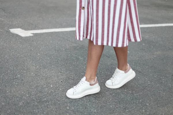 Kaki wanita dengan gaun bergaris-garis merah muda dengan sepatu kulit putih berdiri di jalan di kota. Wanita muda berjalan-jalan. Fashionable sepatu wanita. Koleksi baru. Close-up . — Stok Foto
