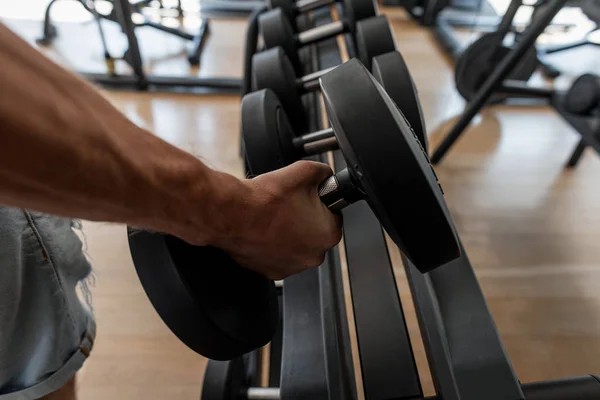 Mano masculina fuerte levantando una mancuerna en un estudio deportivo. El joven atlético entrena en el gimnasio. Primer plano de la mano de un hombre y una mancuerna . — Foto de Stock