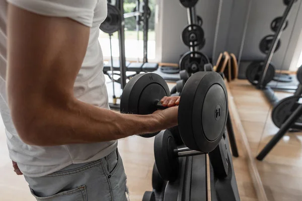 Fuerte joven musculoso haciendo ejercicio en el gimnasio. Primer plano de una mano masculina con una mancuerna . — Foto de Stock