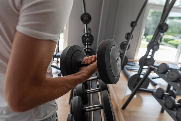 Beyaz moda tişörtlü genç bir spor adamı bir halter alır. Adam spor salonunda antrenman alabiliyorum. Dambıllı bir adamın elinin yakın çekim. — Stok fotoğraf