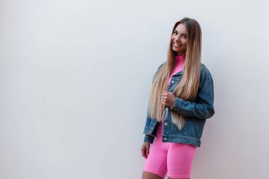 Sevimli gülümseme ile bir kot ceket pembe şort trendy pembe üst Neşeli güzel genç kadın sokakta bir vintage duvar yakınında ayakta rahatlatır. Mutlu sevimli kız modeli açık havada. Retro tarzı.
