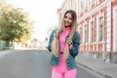 Şık sarı uzun saçlı komik genç kadın şık yazlık giysiler ivedi bir binanın yakınında bir şehirde poz olumlu bir gülümseme ile. Mutlu kız. Yaz stili. Kadın giyim yeni koleksiyonu.