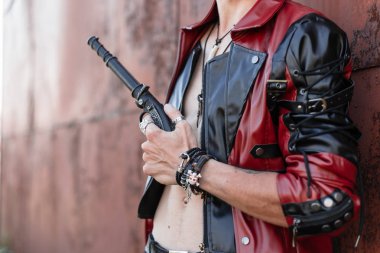 Eski paslı bir duvarın yakınında poz veren bir vintage silah ile siyah bir kot şık bir deri ceket çıplak gövde ile seksi serin genç adam. Eski moda erkek modeli. Close.