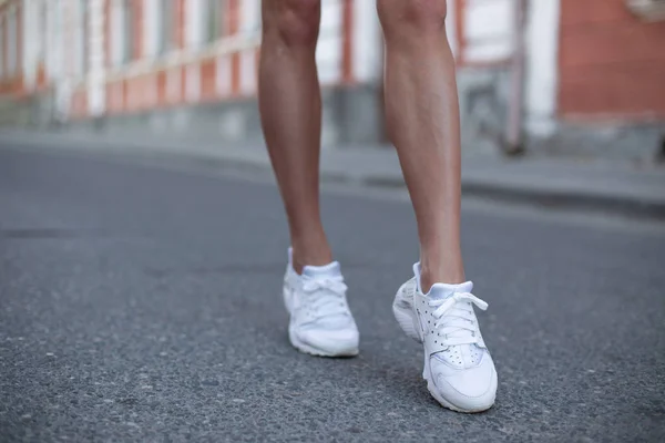 Moderne jonge vrouw met slanke gelooide benen in modieuze sport sneakers staat op de stoep in de stad op de zomerdag. Stijlvolle zomer Womens schoenen. Close-up. — Stockfoto
