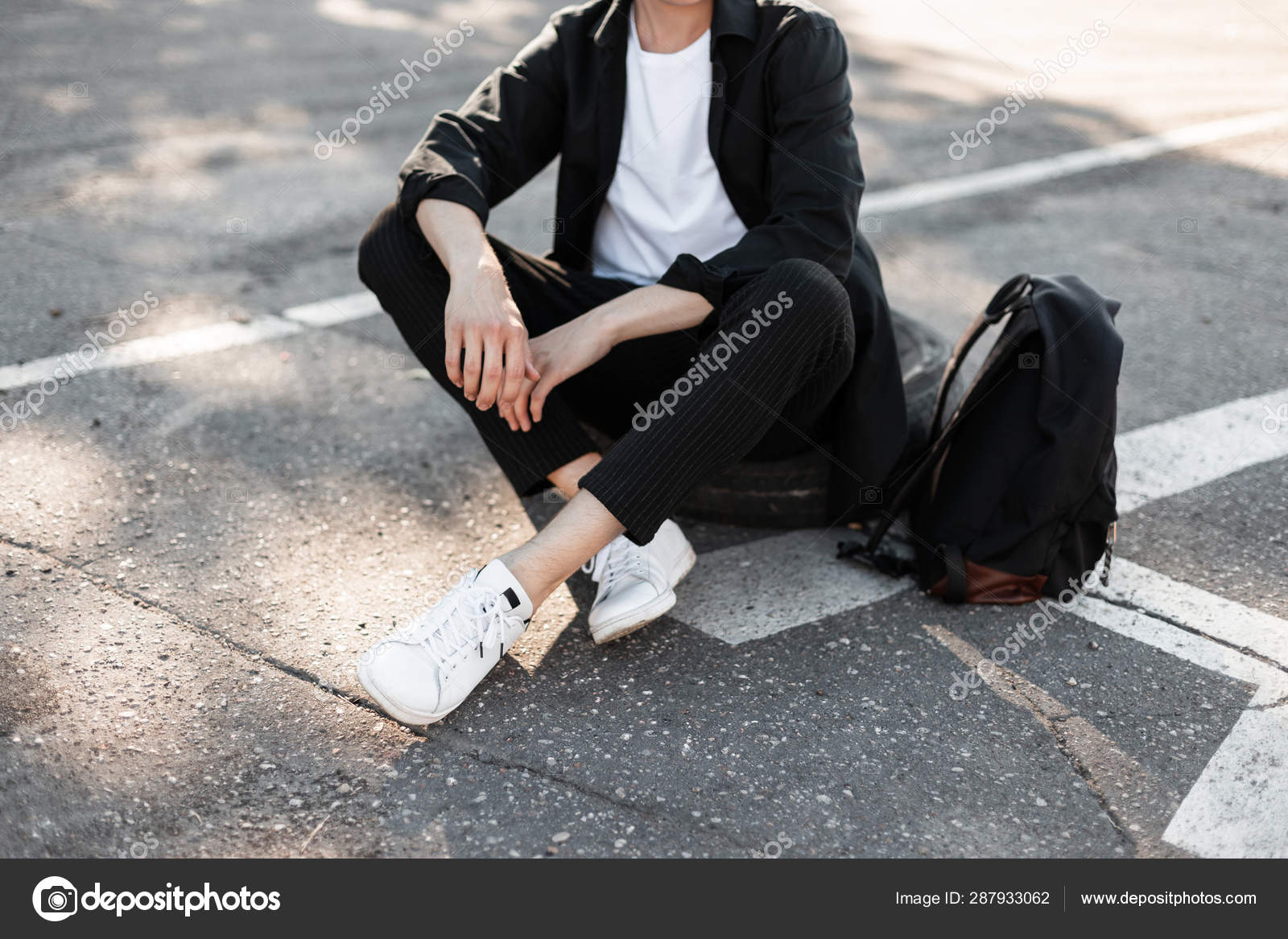 Hombre joven moderno de moda en jeans con estilo en unas zapatillas blancas  de temporada de cuero de moda se encuentra en un estacionamiento en la  ciudad. primer plano de las piernas