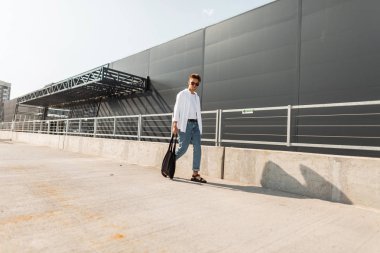 Siyah bir bez çanta ile trendy sandalet şık beyaz ve denim giysiler kentsel genç adam hipster güneşli bir gün açık havada yürür. Şehirde güneş gözlüğü olan yakışıklı adam. Yaz moda erkek giyim.
