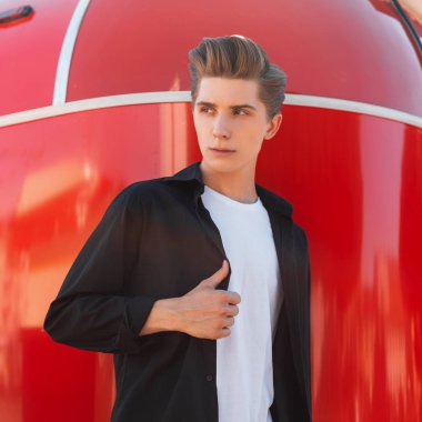 Bir t-shirt bir Vintage siyah gömlek şık bir saç stili ile çekici genç adam güneşli bir günde Metalik kırmızı duvar yakın pozlar. Cool şık adam moda modeli.