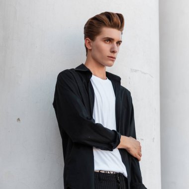Moda bir saç stili ile bir t-shirt trendy siyah gömlek modern şık genç adam sokakta sütunlar ile beyaz bir Vintage bina yakın pozlar. Zarif adam moda modeli. Şık erkek giyim.