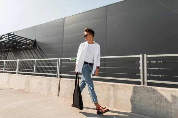Amerykański Hipster młody mężczyzna w okulary przeciwsłoneczne w stylowe letnie ubrania z tkaniny torba w rocznika sandały spacery na ulicy w słoneczny dzień. Przystojny facet. Nowa kolekcja modnych ubrań dla mężczyzn. — Zdjęcie stockowe