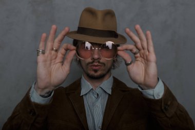 Eski moda genç adam hipster zarif giysiler içinde şık bir şapka bir sakallı kamera bir vintage yuvarlak pembe gözlük gösterir. Odada seksi erkek modeli. Batı retro tarzı. Gözlüklere odaklanın.