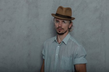 Şık bir gömlek retro tarzı zarif bir şapka sakallı yakışıklı genç adam bir vintage gri duvar yakınında stüdyoda duruyor. Çekici acımasız hipster adam. Retro tarzı. Moda erkek giyim