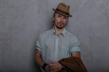 Kot pantolon zarif bir gömlek kahverengi bir şapka ile deri bilezik ile Ciddi yakışıklı genç hipster adam duvara yakın odada duruyor. İçeride seksi sakallı adam var. Eski moda stil