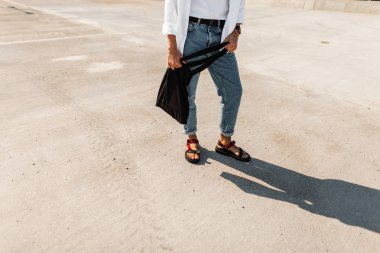 Kaldırımda siyah kumaş çanta standı ile şık kırmızı deri sandalet mavi vintage kot Trendy erkek bacakları. Erkek giyim ve ayakkabı moda yeni yaz koleksiyonu. Close