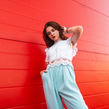 Kırmızı ahşap duvara yakın şehirde poz moda blues pantolon vintage dantel beyaz üst Pretty modern genç kadın modeli. Zarif kız esmer açık havada. Şık kadın yazlık giysileri.