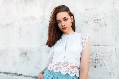 Kahverengi saçlı zarif giysiler içinde Pretty moda genç kadın model vintage beyaz duvar yakınında şehirde pozlar. Modern