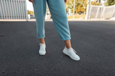 Asfalt üzerinde şık deri spor ayakkabı mavi vintage pantolon kadın bacaklar Closeup. Yürüyüşte modaya uygun bir kadın. Şık spor ayakkabıların modern mevsimlik koleksiyonu. Kadın modası.