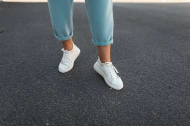 Şehirde asfalt üzerinde beyaz deri spor ayakkabı şık mavi pantolon Kadın bacaklar. Yürüyüşte modaya uygun genç kadın. Modaya uygun kadın ayakkabıları. Yeni koleksiyon. 