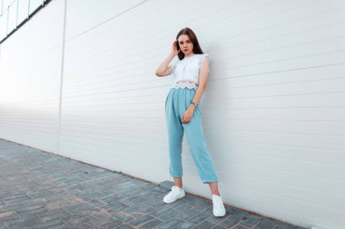 Beyaz spor ayakkabı mavi pantolon şık bir dantel üst güzel genç kadın model şehirde modern bir binanın yakınında duruyor. Dışarıda güzel bir kız var. Kadın giyim trendy yaz koleksiyonu.